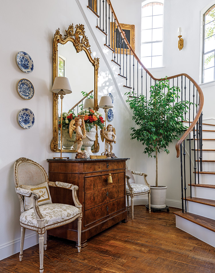 Kristie Shelton’s entryway at her home in Richland Hills, Texas is adorned in her favorite French antiques, including a gilt mirror and a pair of chairs flanking a chest. The staircase leading to the second floor was remodeled to Kristie’s sleeker, more elegant taste.