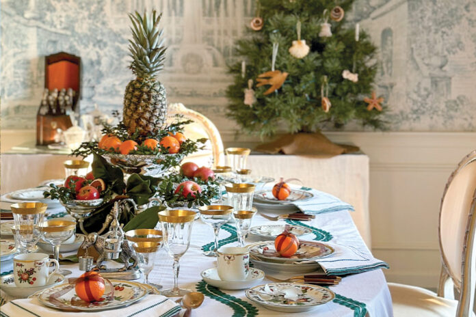 Jenny Bohannon’s dining room features a Christmas tablescape. Green-trimmed Julie Amory linens cover the table laid with Mottahedeh’s Duke of Gloucester china and gold-rimmed glassware. Fresh fruit and greenery in silver holders make up the centerpieces.