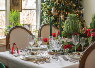 Crystal for Christmas: Crystal wine and water goblets are set on a dining table decorated for a holiday party. A decorated Christmas tree twinkles behind the table.