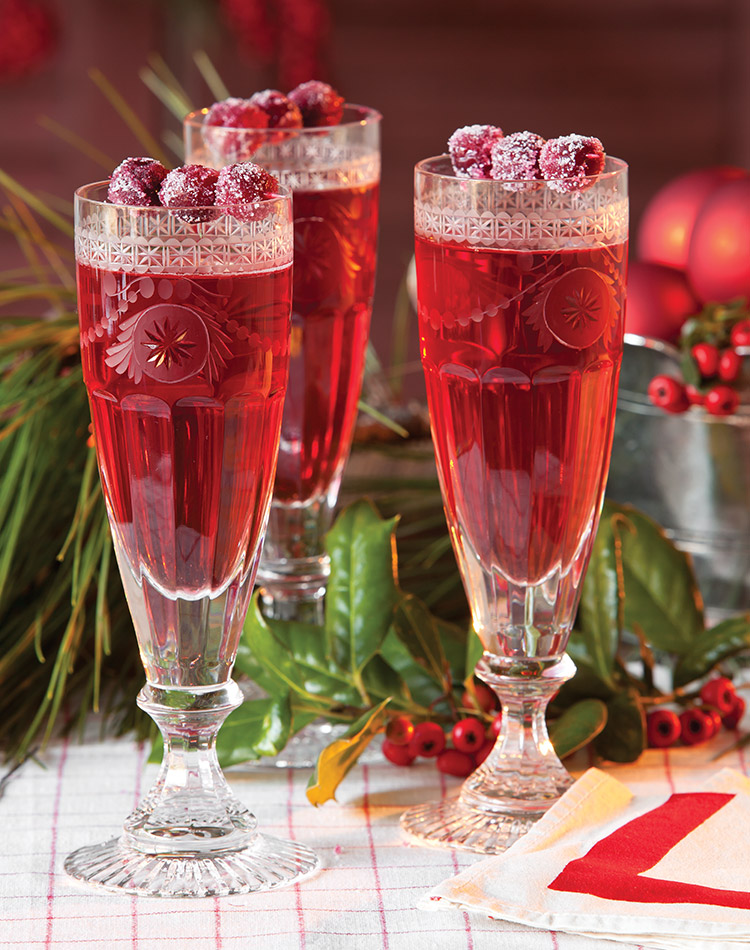 Glass flutes full of ruby red cranberry cocktail, garnished with candied cranberries.