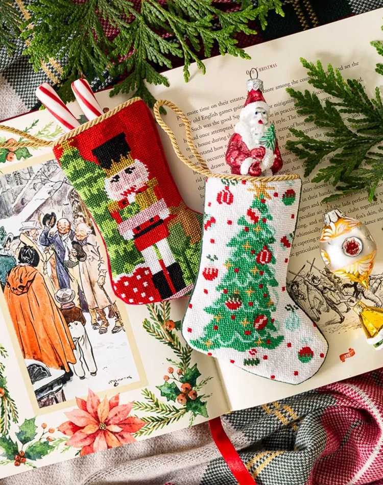 Lying atop an open Christmas book, two hand-stitched needlepoint stockings from Bauble await the quaintest and yet most thoughtful of gifts. 
