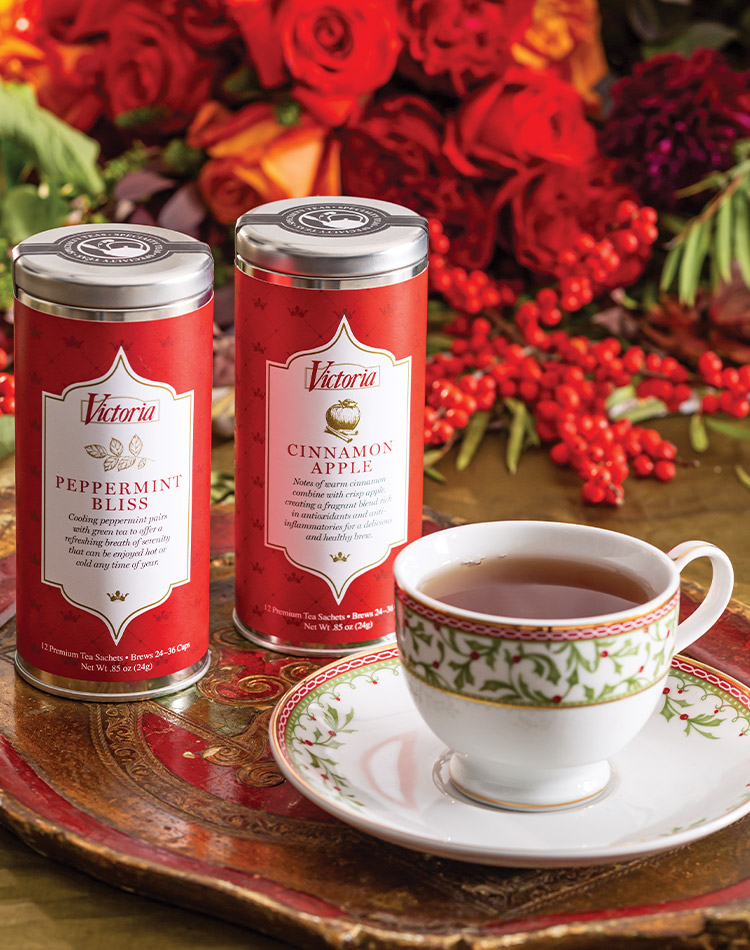Our duo of crimson-wrapped Holiday Tea Tins sits beside a brewed cup in a classic Christmas china pattern.