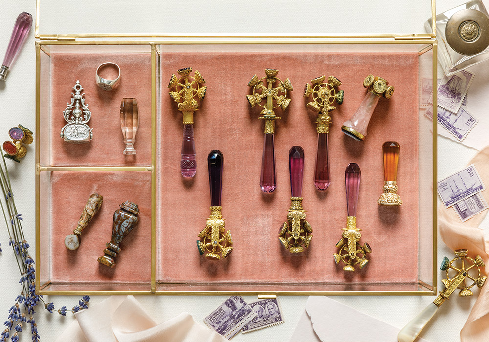 A golden box with a pink velvet base is home to a collection of intricate wax seals.