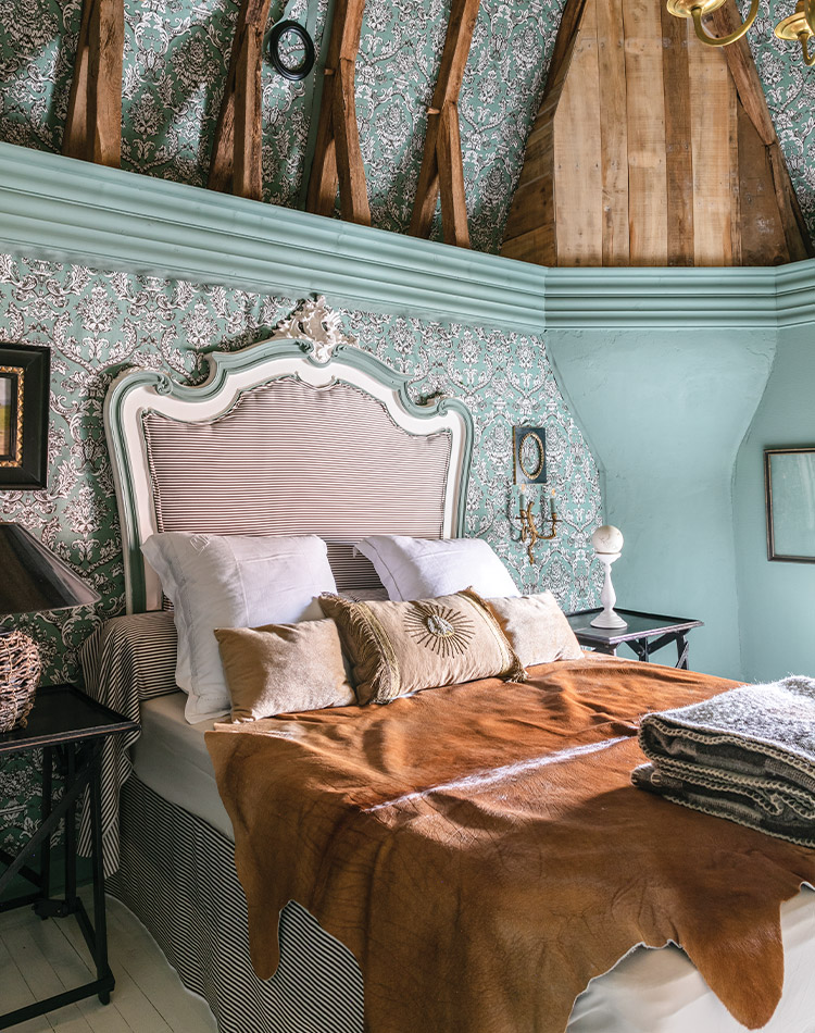 Tall, intricate ceilings lend historic charm to this unique French bedroom, adorned with teal paint and rustic touches. 