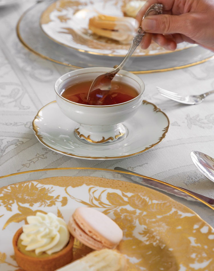 A hand reaches with a small silver spoon to stir a cup of tea.