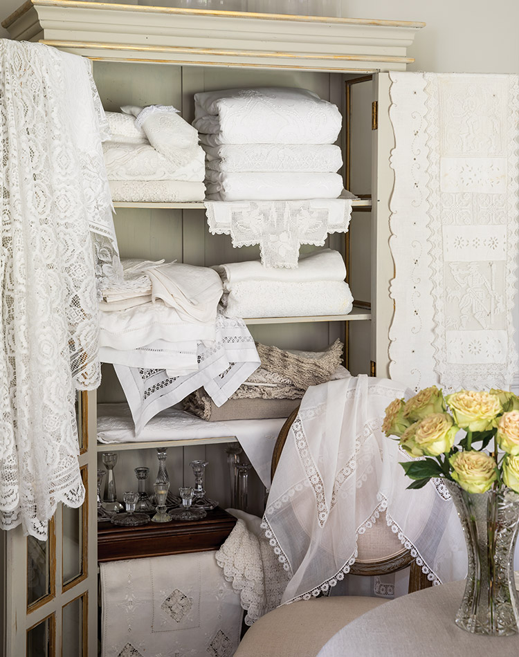 An ivory cupboard spills with lace-kissed linens.