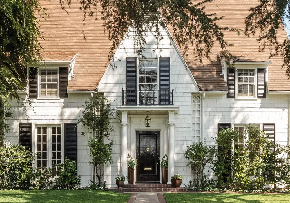 Lush vegetation welcomes guests to Leslie Saeta’s white shingled house in Southern California. A black front door and matching shutters are classic design elements that complement this early twentieth-century home.