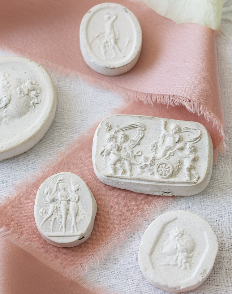 Displayed atop a pink ribbon, these antique intaglios are made from plaster and add historic charm to any space.