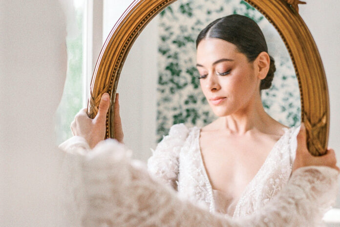 Wedded Bliss: 9 Ways to Add Romance to Your Wedding Events. A lovely bride clad in a delicate lace gown gazes into a gilt-edged mirror.