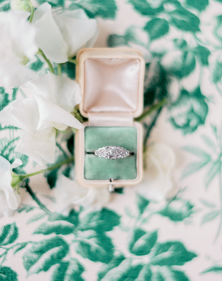 An antique diamond engagement ring sparkles from its nesting place against fern-green velvet in an ivory ring box.