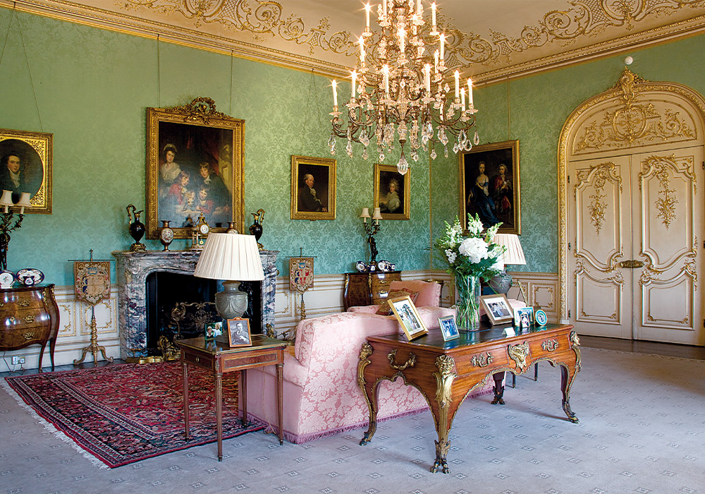 A pink sofa, gold-framed portraits, and a crystal chandelier dress this room in Highclere Castle with fine history.