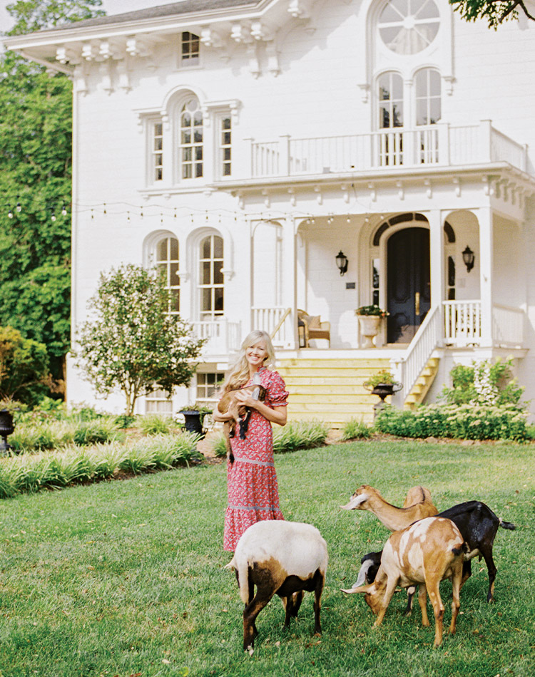 Casey Cashell cradles a baby goat in front of the beautiful main house at Mayhurst Estate.