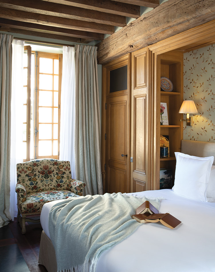 Natural wood surfaces and white linens dress this sunlight-speckled hotel room at La Borde en Sologne Château & Spa.