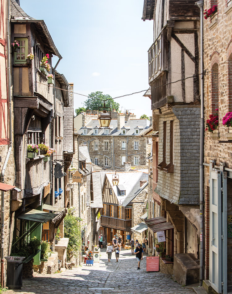 Standing at the top of a hill, looking down the quaint streets of Dinan, a view of flower boxes in windows and pedestrians meandering from shop to shop feels like stepping into a storybook.