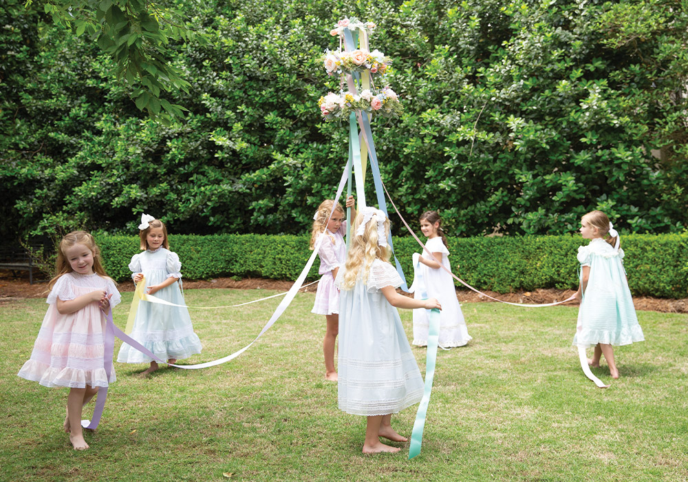Girls in heirloom dresses circle a flower-bedecked maypole.