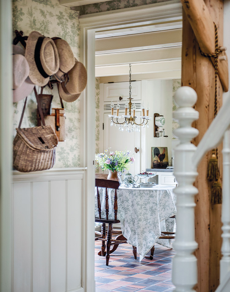 A mingling of hats and crossbody bags hang from the wall near this staircase, while a view through to the dining area offers French charm.