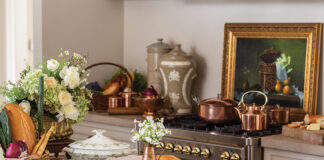 A selection of breads and cheeses nestle among fresh floral arrangements and pretty dishware in a French kitchen.