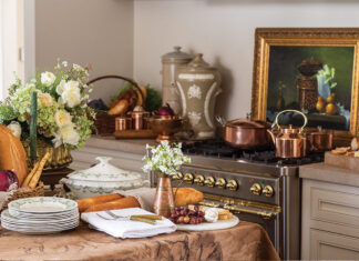 A selection of breads and cheeses nestle among fresh floral arrangements and pretty dishware in a French kitchen.