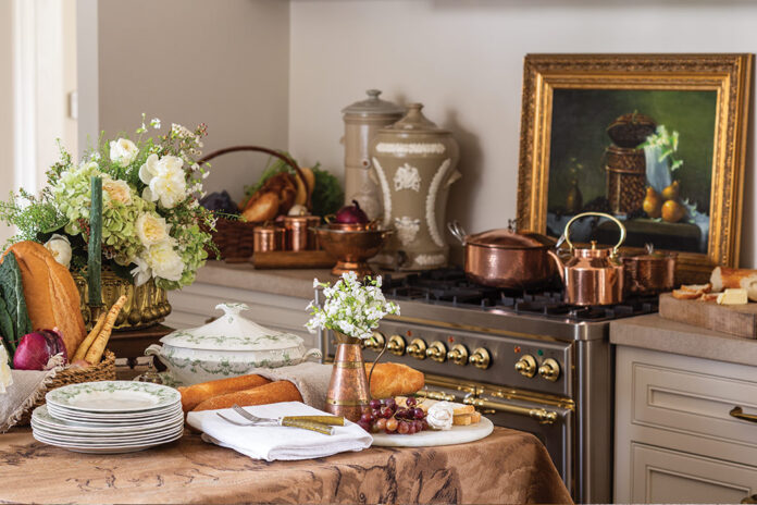 A selection of breads and cheeses nestle among fresh floral arrangements and pretty dishware in a French kitchen.