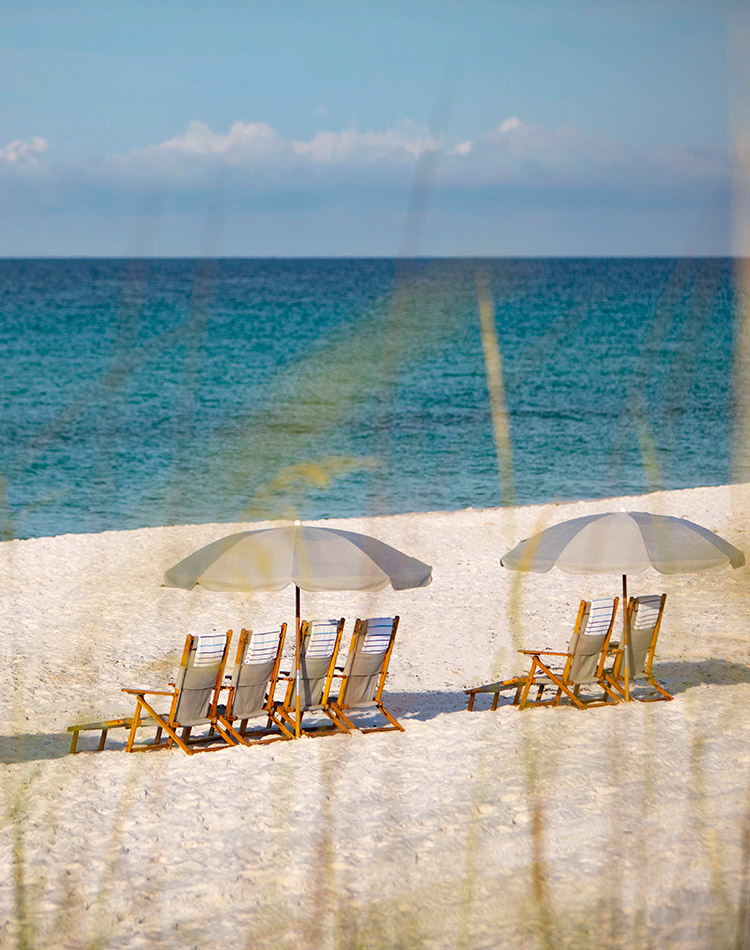 Cushioned beach chairs lounge under wide umbrellas, beckoning visitors to sit a while and enjoy the turquoise tide.