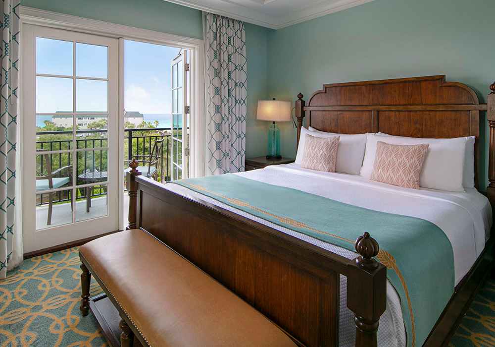 A bed made in blankets matching the seaside view seen through white bay doors. 