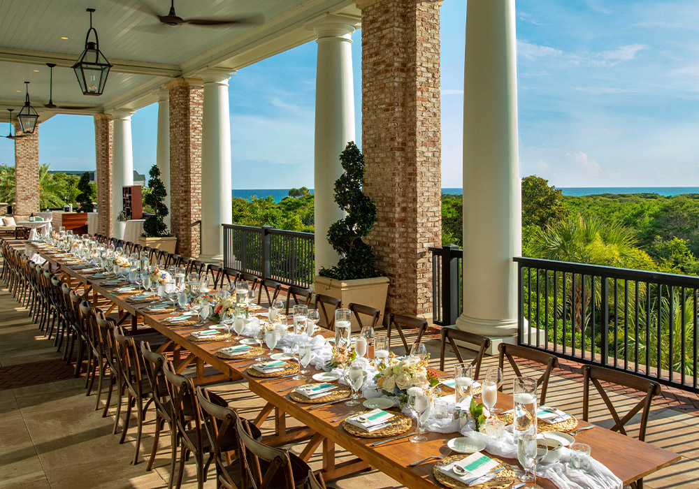 A long and lavish table at he resort’s signature restaurant, Primrose, is set for guests and boasts ocean views beyond an emerald canopy of coastal trees.