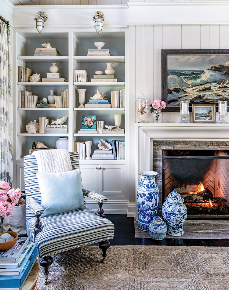 A seaside theme of blue-and-white décor graces this living room, where a cozy fire roars and seashells don the bookshelves.