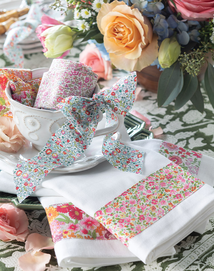 Mirroring the flowers placed nearby, an assortment of Liberty fabrics—both stitched into napkins and tied into ribbons on the handle of a teacup—evokes thoughts of a wildflower field in summertime.