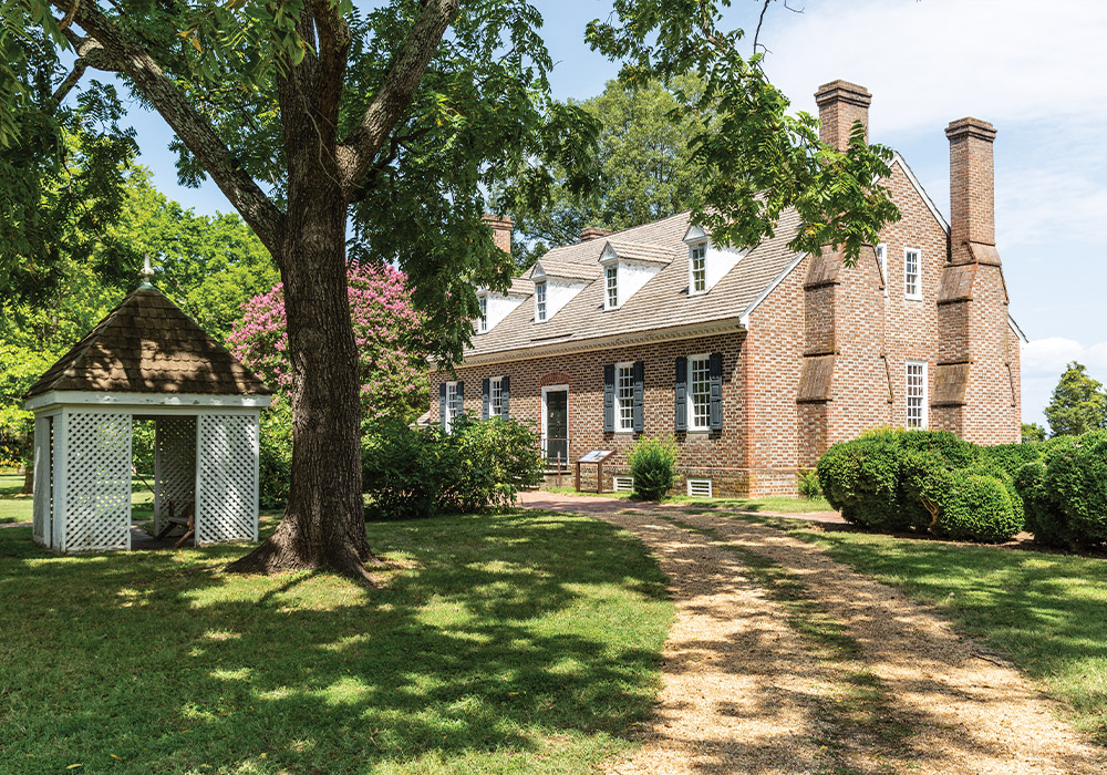 The house at Wakefield is a beautiful, symmetrical red brick structure shaded by a great tree in this image.
