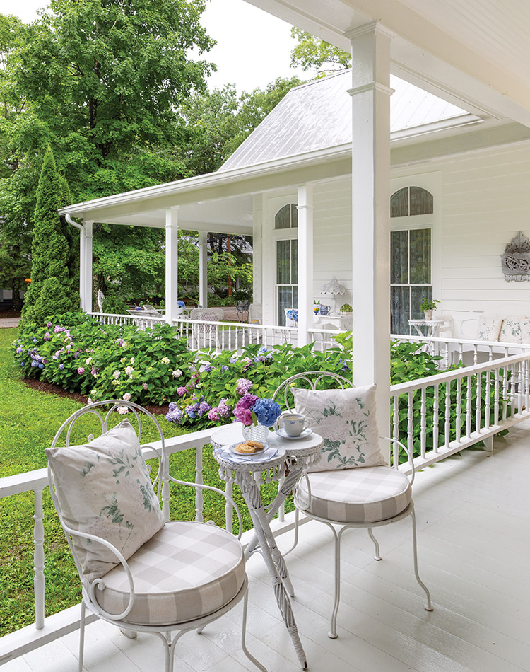 An open wrap-around white porch is set for two to enjoy the summer afternoon.