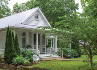 A white cottage overlooks a lush green lawn in our Romantic Cottage 2024 issue.