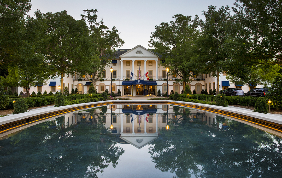 The stately facade of the Williamsburg Inn reflects in a still pool under an early evening sky.