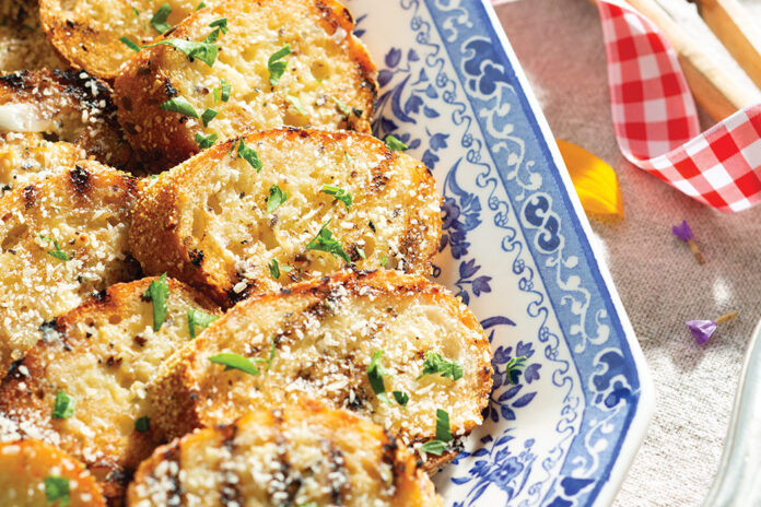 Grilled Garlic Bread is the perfect complement to a lakeside gathering. Each crunchy and buttery slice is a delicious vehicle for several summertime dishes. The smoky kiss from the char is a reminiscent and nostalgic flavor of summer.