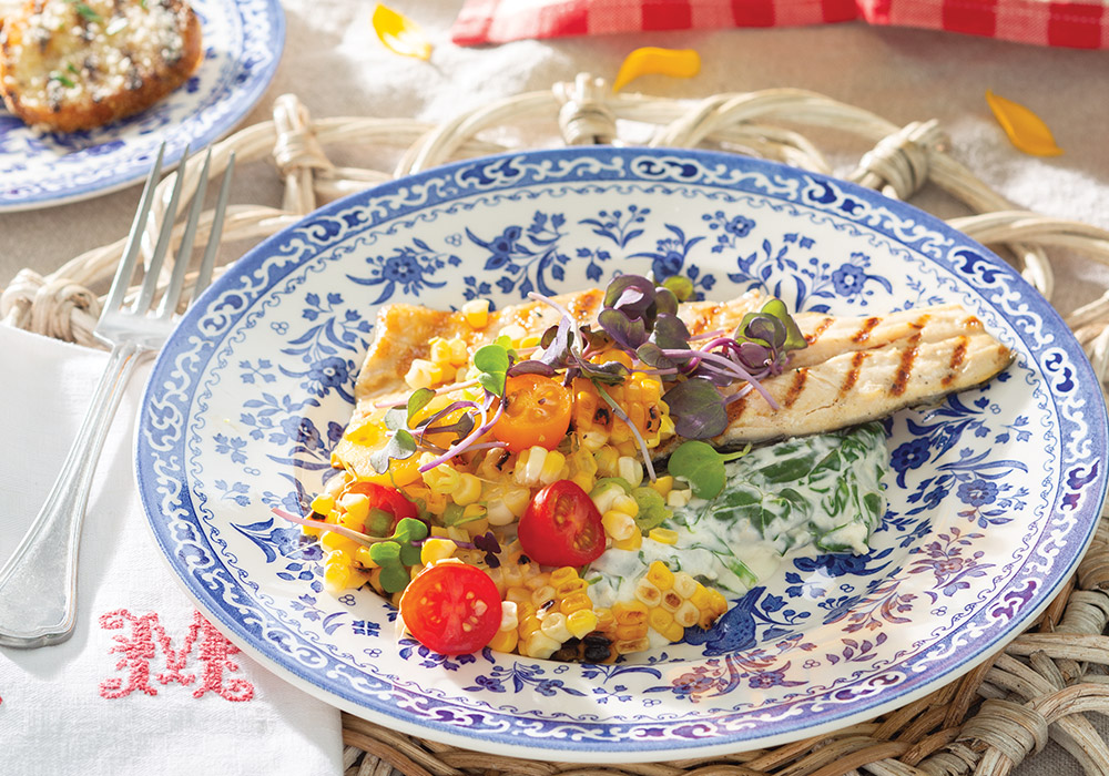 Grilled trout with corn-and-tomato salsa and creamed spinach on a blue-and-white china plate.