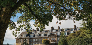 The exterior of Gleneagles resort can be seen framed by a grassy knoll and shady boughs.