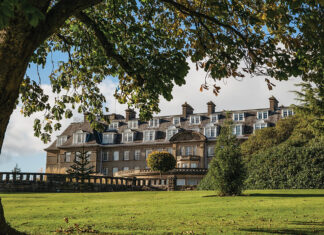The exterior of Gleneagles resort can be seen framed by a grassy knoll and shady boughs.