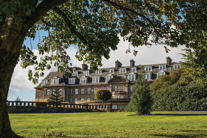 The exterior of Gleneagles resort can be seen framed by a grassy knoll and shady boughs.
