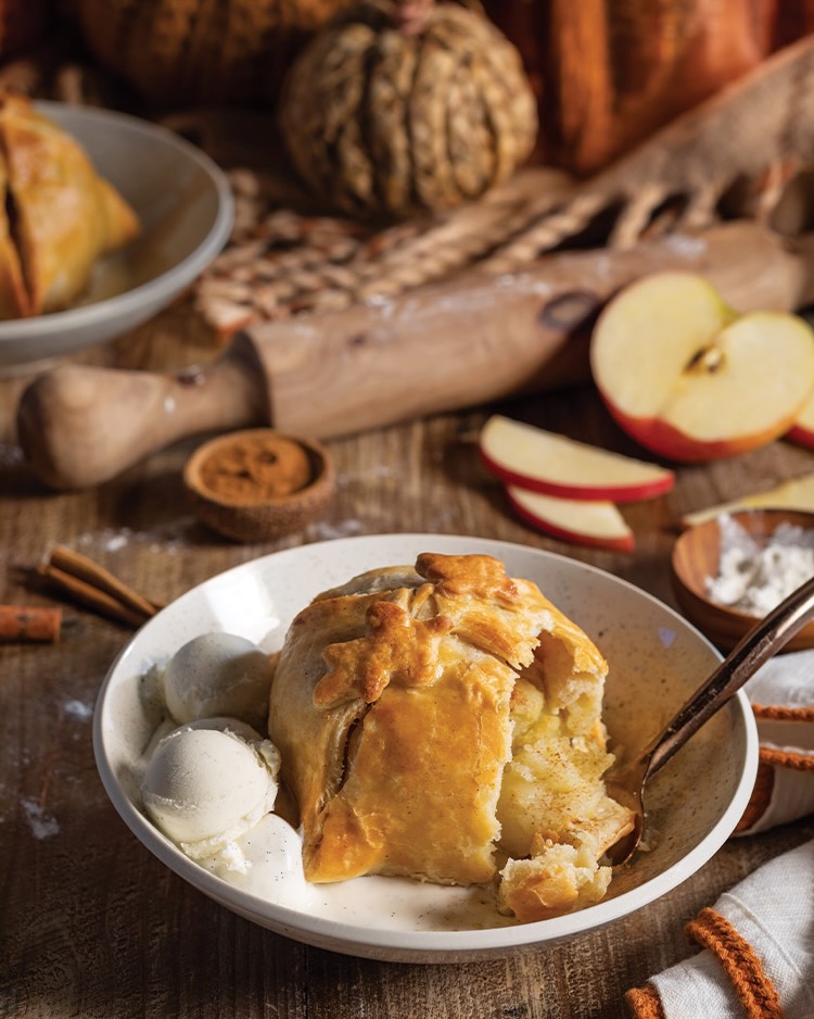 Two scoops of vanilla ice cream and a perfectly golden brown baked Apple Dumpling are served at this fall table.