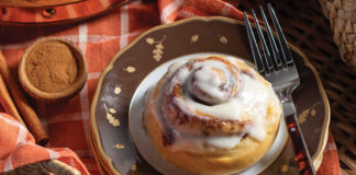 A single serving of a cinnamon roll waits on an autumnal stack of plates.