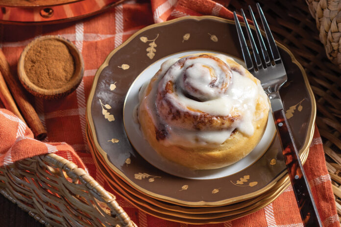 A single serving of a cinnamon roll waits on an autumnal stack of plates.