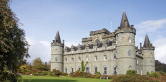The green facade of Inveraray Castle in Scotland is silhouetted against a bright blue sky.