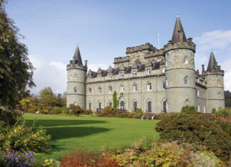 The green facade of Inveraray Castle in Scotland is silhouetted against a bright blue sky.