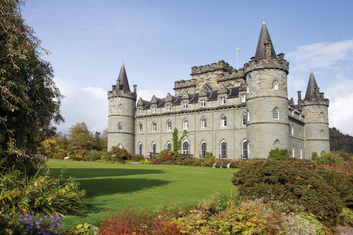 The green facade of Inveraray Castle in Scotland is silhouetted against a bright blue sky.