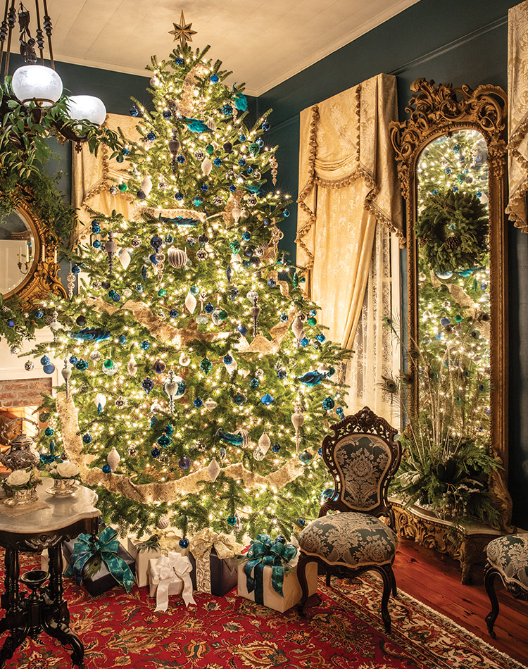 In the formal parlor of this historic home, a set of mid-nineteenth-century furniture boasts traditional damask upholstery in a non-traditional hue. This was the inspiration for the custom paint color and crowd-pleasing contemporary Christmas tree covered in blue-and-silver ornaments, ivory ribbon, and peacock plumes.