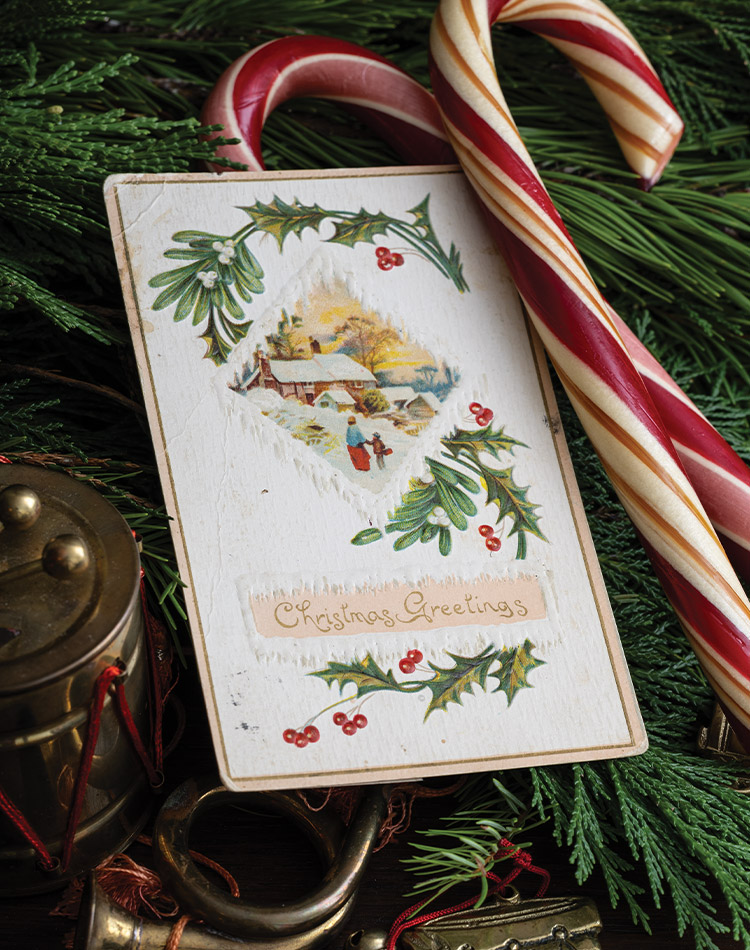 Crossed candy canes and evergreen boughs offer a seasonal backdrop for this displayed antique Christmas card.]