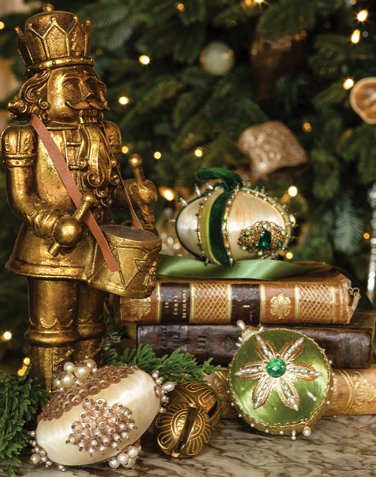  A golden nutcracker and breathtaking hand beaded ornaments are displayed on a table beside a glowing Christmas tree.