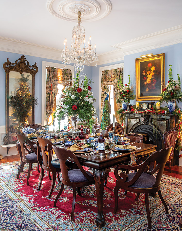 Pale blue walls and a breathtaking ornate rug in this dining room are lovely any time of year, but the vibrant evergreen and crimson flowers atop the table and mantel bring out the best at Christmas