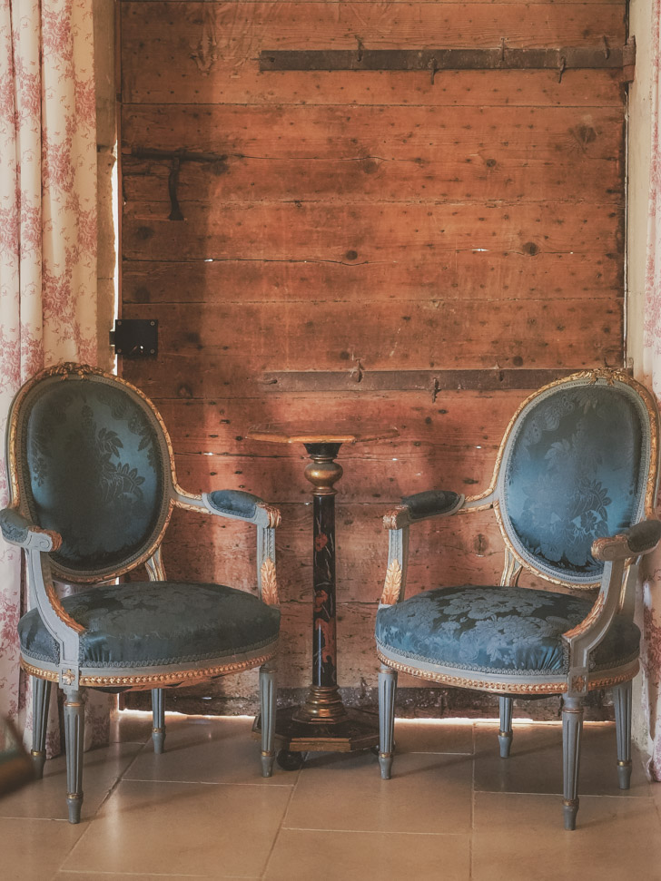 Antique blue chairs in front of a wooden wall.