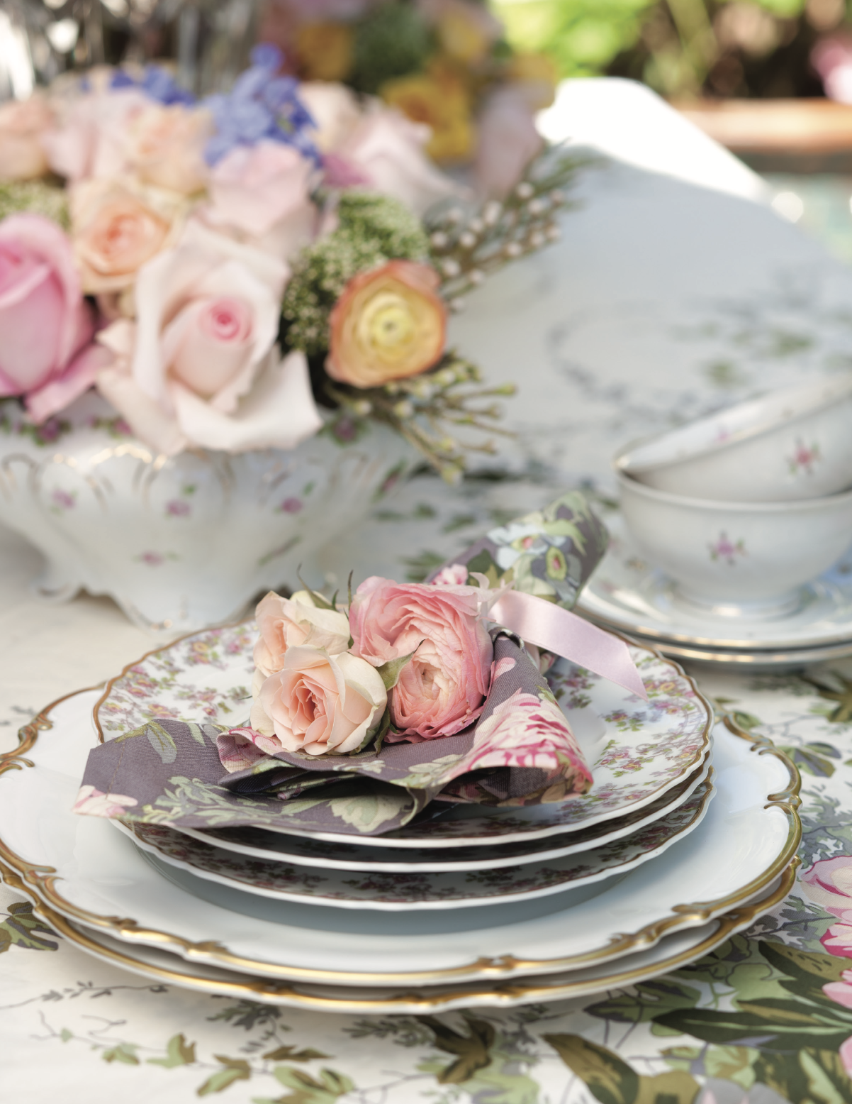 Floral china plates stacked on a table an topped with flowers.