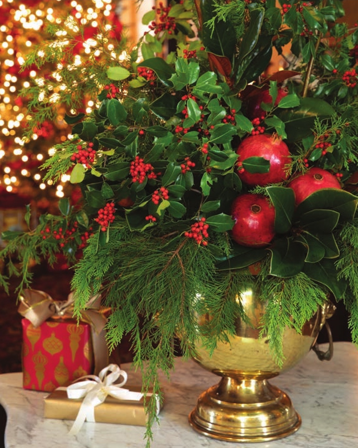 A floral arrangement accented with pomegranates, holly, and evergreen sprigs in a brass vase.